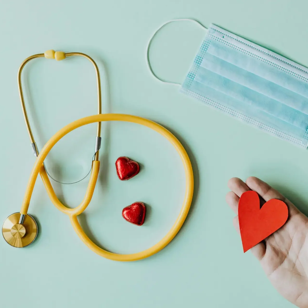 Out of Hours Top view of crop anonymous person hand with red paper heart on table with stethoscope and medical mask for coronavirus prevention